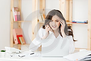 Serious well-dressed saleswoman talking on phone in office behind her desk and laptop computer. Copy space