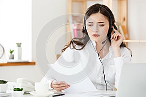 Serious well-dressed saleswoman talking on phone in office behind her desk and laptop computer. Copy space