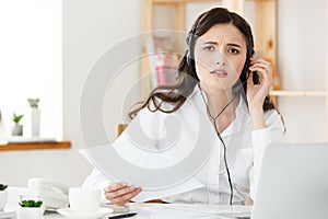 Serious well-dressed saleswoman talking on phone in office behind her desk and laptop computer. Copy space