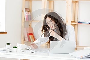 Serious well-dressed saleswoman talking on phone in office behind her desk and laptop computer. Copy space