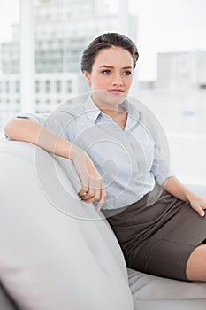 Serious well dressed young woman sitting on sofa