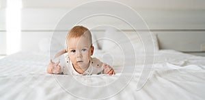 serious white caucasian baby boy with blue eyes six months old lying on the bed and looking at the camera. straight view