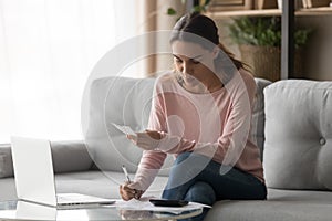 Serious woman calculating domestic bills writing notes at home