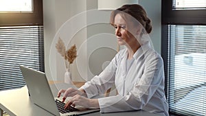 Serious woman doctor in white coat working typing on laptop computer looking on display screen.
