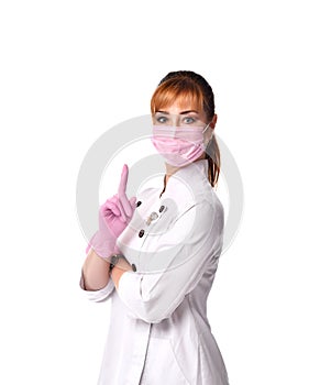 Serious woman doctor in white robe, pink disposable mask and gloves looking at camera pointing finger up.