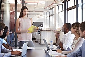 Serious woman with document stands addressing team meeting