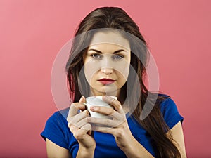 Serious woman drinking coffee over pink background