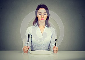 Serious woman with fork and knife sitting at table with empty plate