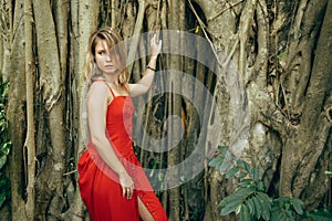 Serious woman in long red dress on background of tree trunks for walk