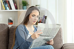 Serious woman reading a newspaper on a couch