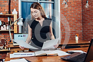 Serious woman reading papers studying resumes standing at work desk in stylish office