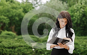 Serious woman reads working book on the background of summer park. The concept of remote work