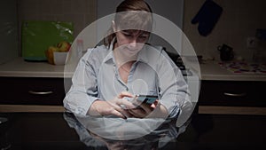 serious woman sitting in the kitchen at night and using the phone