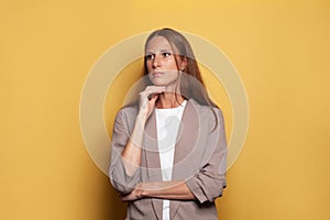 Serious woman standing against yellow studio wall background