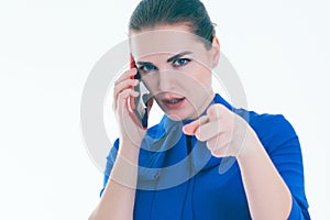Serious woman talking on mobile phone and points a finger at you. Isolated on white.