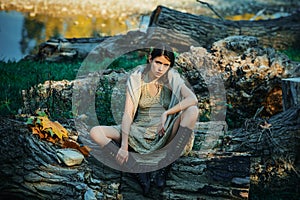 Serious woman on trunk wood. Adult girl relaxed sitting on wood in an outdoor park. Portrait of a beautiful charming