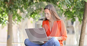 Serious woman uses a laptop on a bench