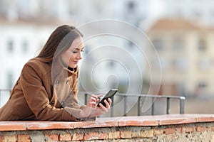 Serious woman using a mobile phone in winter in a balcony