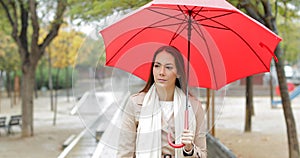 Serious woman walking under the rain in a park