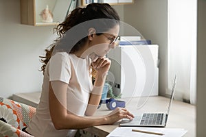 Serious woman wearing glasses using laptop, working on project