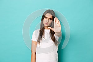 Serious woman in white t-shirt telling to stop, saying no, stretching one hand to prohibit something bad, standing over