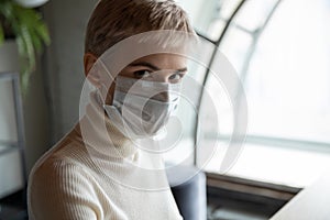 Serious worried 30s female employee in facemask looking at camera.