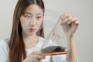 Serious, worried asian young woman, girl holding brush, show her comb, hairbrush with long loss hair problem after brushing, hair