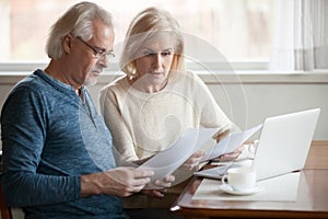 Serious worried senior couple reading documents calculating bill