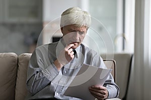 Serious worried senior retired man reading document, paper letter