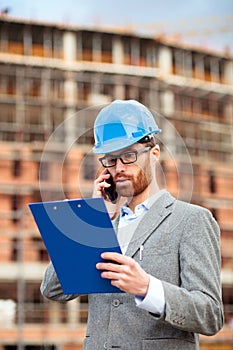 Worried young businessman or architect standing on a construction site and talking on the phone