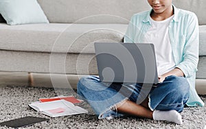 Serious young african american girl studying remotely, typing on laptop, sitting on floor at home interior
