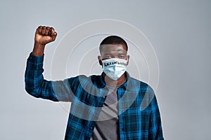 Serious young african american guy wearing protective mask with inscription BLM looking at camera, posing with raised