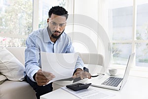 Serious young African American man calculating expenses