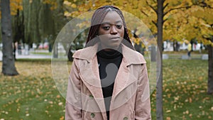 Serious young african american woman standing in park posing outdoors looking at camera shaking head negative response