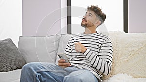 Serious young arab man doubting his next idea, deeply immersed while texting on his smartphone, sitting solo on the living room