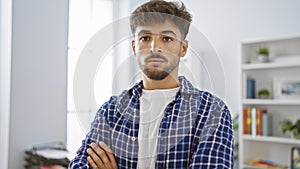 Serious young arab man stands with arms crossed in office, a successful professional worker exuding confidence in his business