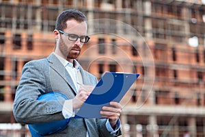 Serious young architect signing paperwork after inspection of a construction site