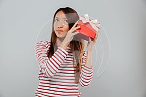 Serious young asian lady standing isolated holding gift.