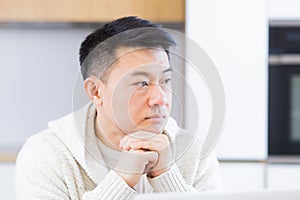 serious young asian man looking away. student writer sit at home office desk with laptop thinking of inspiration search