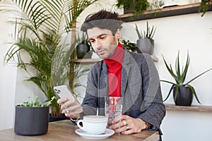 Serious young attractive dark haired businessman dressed in elegant clothes checking his mailbox on smartphone while waiting for