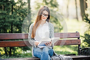 Serious young, beautiful girl holding an open book, read background summer green park