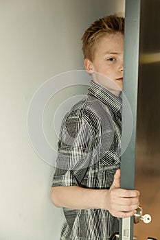 Serious young boy peering around a door