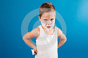 Serious young boy in shaving foam like man holding razor