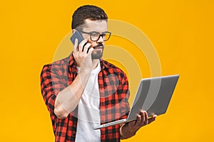 Serious young business man in casual with a laptop sitting at floor calling with smart phone