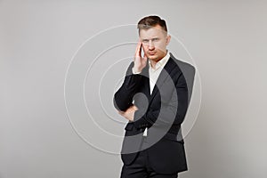 Serious young business man in classic black suit, white shirt putting hand on head, temple isolated on grey wall