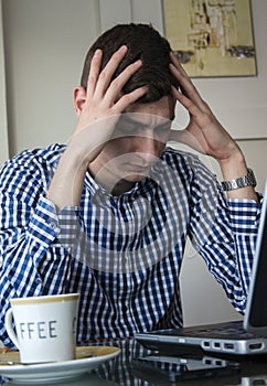 Serious young business man looking worried at laptop screen at home office