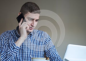 Serious young business man speaking on phone, checking data on screen