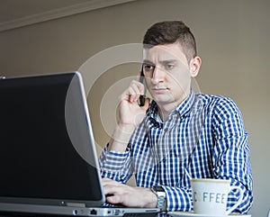 Serious young business man speaking on phone, checking data on screen