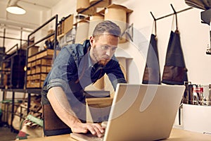 Serious young business owner using laptop in his workshop photo