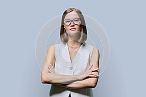 Serious young business woman with crossed arms on grey background